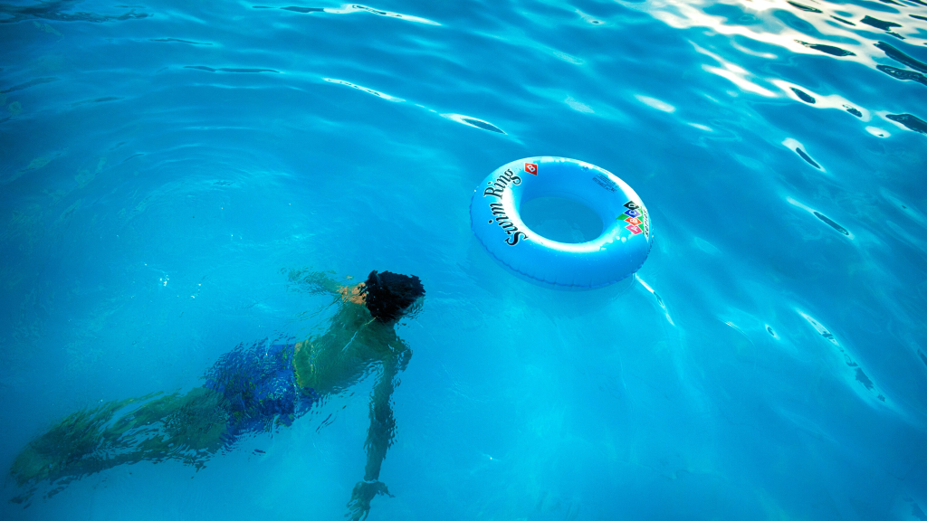 boy in pool swimming towards an inflatable float ring