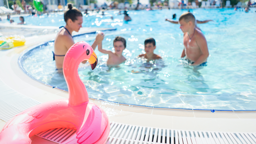 People enjoying time in a public pool and a pink flamingo float in the foreground 